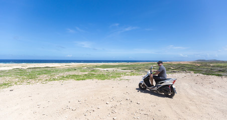 Young man on the Aruba beach on the motorcycle  looking on horizon 