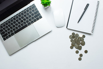 Top view of a modern white desk with a laptop table, smartphone and other accessories with a large amount of coins, a financial note book Accounting concepts.