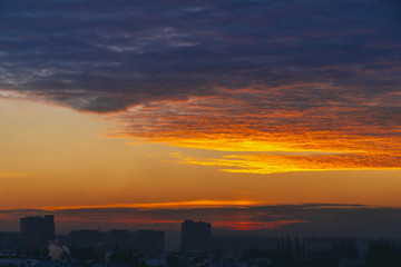 Fototapeta premium Cityscape with wonderful varicolored fiery dawn. Amazing dramatic multicolored cloudy sky. Dark silhouettes of city building roofs. Atmospheric background of sunrise in overcast weather. Copy space.