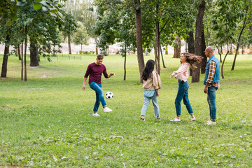happy multicultural group of friends playing football in park