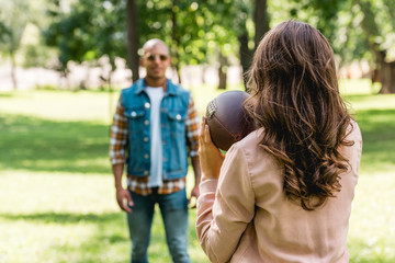 selective focus of girl holding american football and looking at african american boyfriend - Powered by Adobe