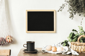 Stylish interior design of kitchen space with small table with mock up frame, herbs, cup of tea, bag with apples and vegetables. Vintage concept of kitchen space..