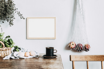 Stylish interior design of kitchen space with small table with mock up frame, herbs, cup of tea,...