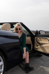 Attractive young woman posing leaning on convertible car