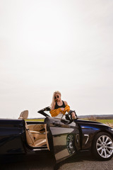 Fototapeta na wymiar Attractive young woman posing leaning on convertible car