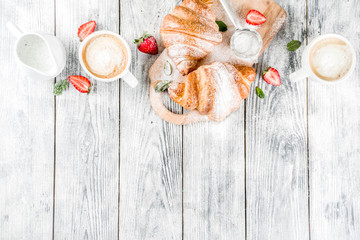 Breakfast concept with coffee cup, croissants, cream and fresh berries. On a light wooden background, top view, copy space