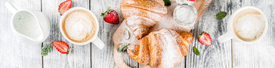 Breakfast concept with coffee cup, croissants, cream and fresh berries. On a light wooden background, top view, copy space