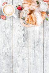 Breakfast concept with coffee cup, croissants, cream and fresh berries. On a light wooden background, top view, copy space