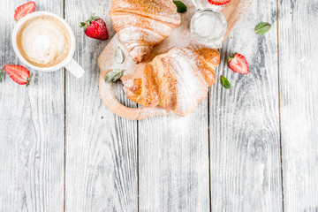 Breakfast concept with coffee cup, croissants, cream and fresh berries. On a light wooden background, top view, copy space