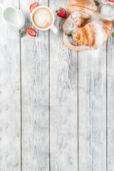 Breakfast concept with coffee cup, croissants, cream and fresh berries. On a light wooden background, top view, copy space