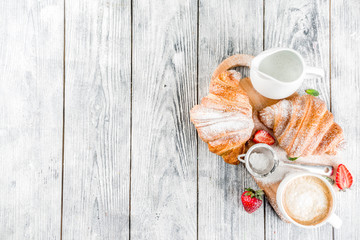 Breakfast concept with coffee cup, croissants, cream and fresh berries. On a light wooden background, top view, copy space