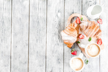 Breakfast concept with coffee cup, croissants, cream and fresh berries. On a light wooden background, top view, copy space