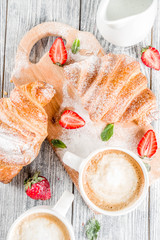 Breakfast concept with coffee cup, croissants, cream and fresh berries. On a light wooden background, top view, copy space