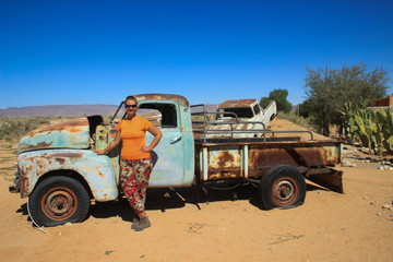 Obraz premium Abandoned old rusty cars in the desert of Namibia and a plump white tourist girl near the Namib-Naukluft National Park. Africa
