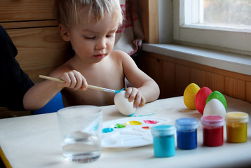 Cute blond son dyeing Easter eggs at home. Candid photo with natural light