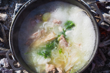 Shurpa soup in a large cast-iron cauldron outdoor. Summer food for hike. Top view.
