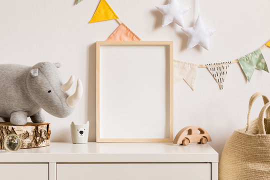 The modern scandinavian newborn baby room with mock up photo frame, wooden car, plush rhino and clouds. Hanging cotton flags and white stars. Minimalistic and cozy interior with white walls.Real photo