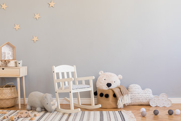 Stylish and modern scandinavian newborn baby interior with toys, children's chair,plush rhino, natural basket with teddy bear and small wooden shelf. Grey background walls with stars pattern.