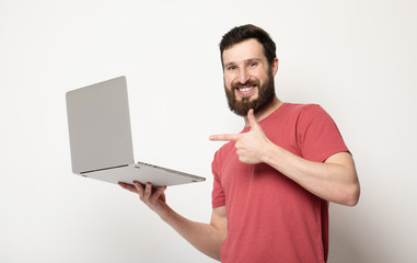 Portrait of a joyful young man in red t-shirt looking at laptop computer and celebrating isolated over grey background 