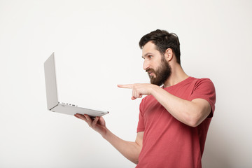 young bearded man looks at laptop screen in his hands and stands isolated on light background 