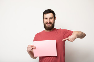 Young bearded man with blank pink banner. Smiling man holding advertising sheet, copy space, isolated 