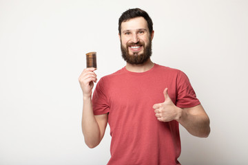 Attractive smiling Bearded man holding a comb for beard standing above grey background