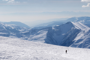Silhouette of skier on snowy off-piste slope and mountains in haze