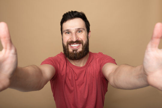Close up photo of beautiful amazing bearded brunette man hold telephone in arms make take selfie wear casual checkered plaid t-shirt outfit isolated on beige background 