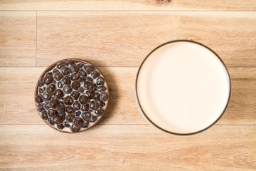 Fototapeta na wymiar A glass cup of pearl milk tea (also called bubble tea) and a plate of tapioca ball on wooden background. Pearl milk tea is the most representative drink in Taiwan. Taiwan food . With copy space.