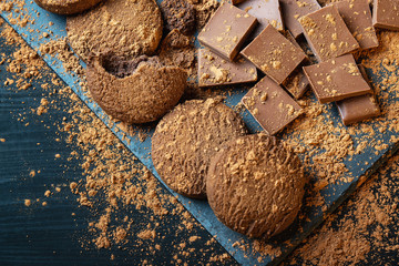 Chocolate chip cookies, broken pieces of chocolate and cocoa powder on a wooden background...