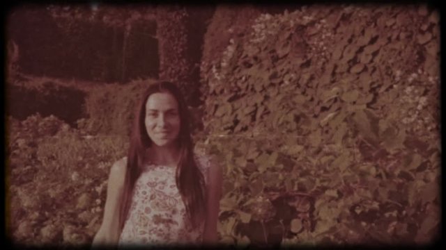 Family video archive. Retro camera 8&nbsp;mm. Old film. Young attractive woman having fun in the green garden. Portrait of a smiling brunette with dimpled cheeks against a green park. Pretty girl in summer