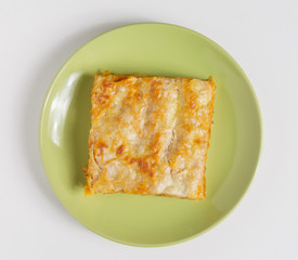 A piece of lasagna on a plate on a white background.