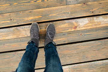 Women's legs in stylish suede boots stand on a bridge of wooden planks on a cold, winter day.