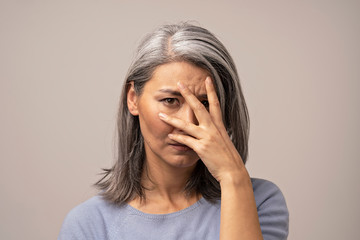 Woman of Mongolian Appearance with a Sad Look on a Gray Background.