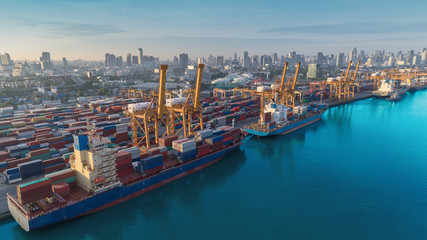 Aerial view Container ship at sea port and working crane bridge loading container with cityscape...
