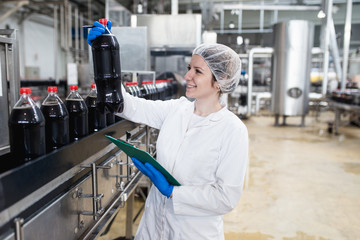 Young happy female worker in bottling factory checking juice bottles before shipment. Inspection quality control.