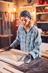 Fototapeta na wymiar Woman carpenter sanding old window in a retro workshop.