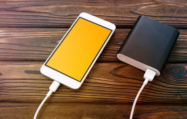 Smartphone with yellow screen, charger on wooden background. technology, Internet.