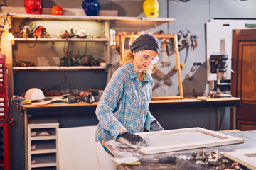 Woman carpenter sanding old window in a retro workshop.