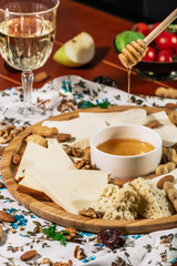 Cheese plate and chef hand wich pours honey: Sulguni, Guda, cheddar, gouda, camembert, and other served with white wine, honey and nuts on wooden board on light background. Tasty appetizers.