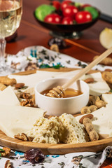 Assorted cheeses on round wooden board plate served with white wine Guda cheese, cheese grated bark of oak, hard cheese slices, walnuts, grapes, crackers, honey, sulguni, light wood background