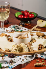 Assorted cheeses on round wooden board plate served with white wine Guda cheese, cheese grated bark of oak, hard cheese slices, walnuts, grapes, crackers, honey, sulguni, light wood background