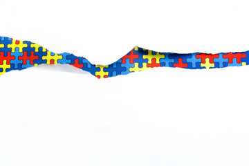 torn white paper on multicolored puzzle background. Cocept for autism awareness day. Break barriers together for autism.