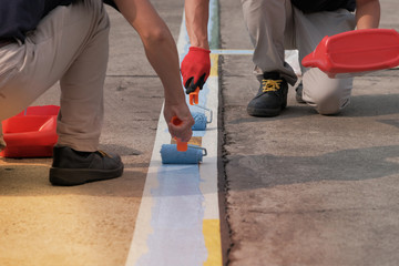 Specialist painters working together for painting blue lines striping on concrete floor of parking lots in car park. Profestional painter man at work with a roller, Blank for text with copy space. © Nudphon