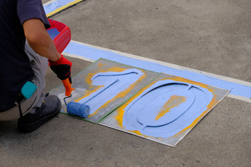 A painter painting parking lots blue lines striping in a car park.