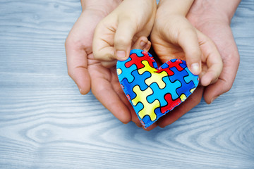 World Autism Awareness day, puzzle or jigsaw pattern on heart with autistic child's and father hands