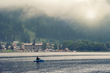 travel and tourism. summer landscape on the lake, fisherman sitting in a small wooden boat fishing. on the lake village, over the mountains fog.