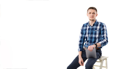 A young Caucasian man with a tablet in his hands is sitting on a white isolate background. Theme portrait of a man, an employee is a sales manager salesman with a technology computer in his hands