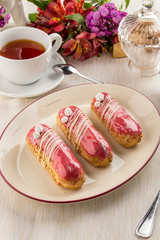 bright pink eclairs with fruit berry filling with tea cup on textile napkin