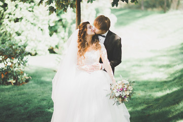 Stylish couple of happy newlyweds walking in the park on their wedding day with bouquet